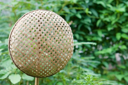 Brown wicker bamboo basket hanging on bamboo stick have blur green leaves as background with copy space.