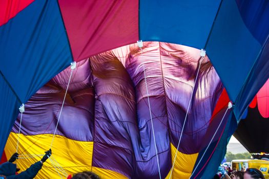 Ground crew holds guys whil the burner inflates this colorful hot air balloon