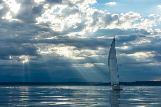 Magic rays penetrate clouds at sunset behind sailboat.