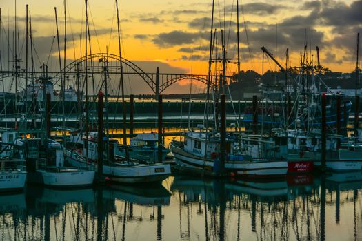 Sun setting in Newport, Oregon over the city's iconic bridge with the fishboat marina in the foreground