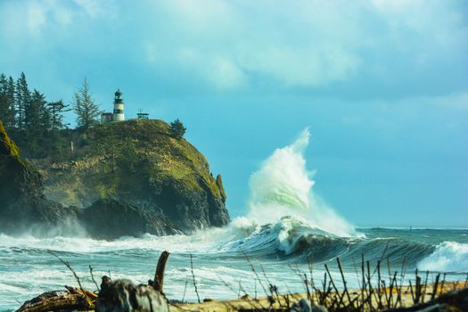 Waves breaking on Waimea Beach at Cap Disappointment with lighthouse in the background.