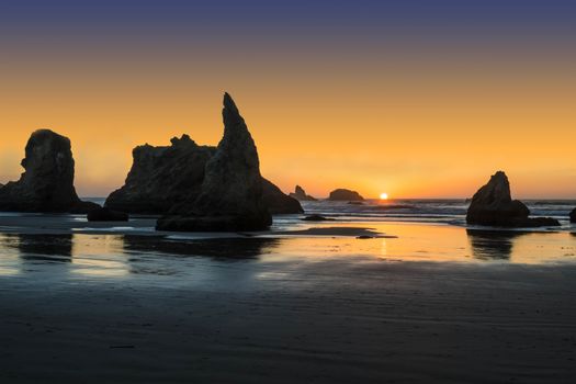 Sun on the horizon in Bandon, OR, behind Wizard's Hat.