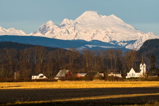 Snow capped Mount Baker across open field with church in the middle ground