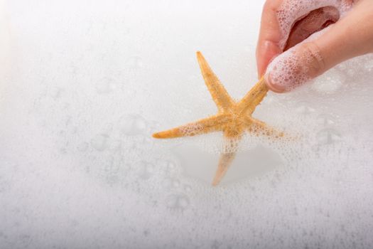 Hand holding starfish in water covered with foam