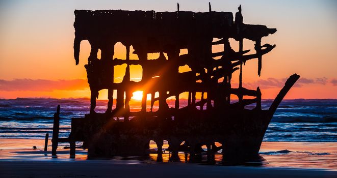 Sun setting behind the wreck of the Peter Iredale on the beach in Fort Stephens State Park, Oregon