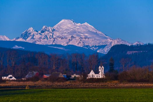 Sun setting on Mount Baker from Skagit Valley with church in foreground