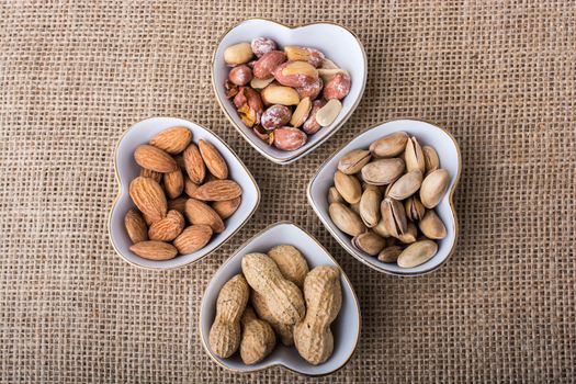 Peanuts, almonds, pistachio  in heart shaped plates on canvas