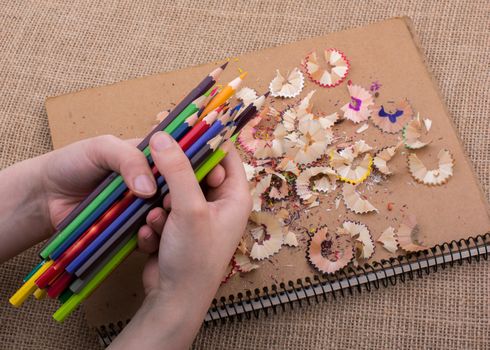 Hand holding Color Pencils over a notebook with pencil shavings