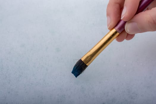 Hand holding a paint brush on water covered with foam