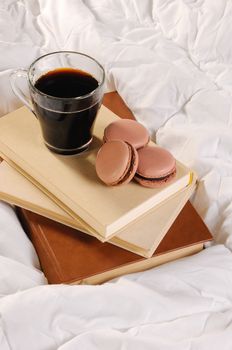 Morning cup of coffee with chocolate cakes Macaroons, on a pile of books in bed.