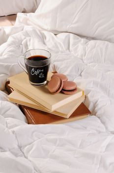 Morning cup of coffee with chocolate cakes Macaroons, on a pile of books in bed.