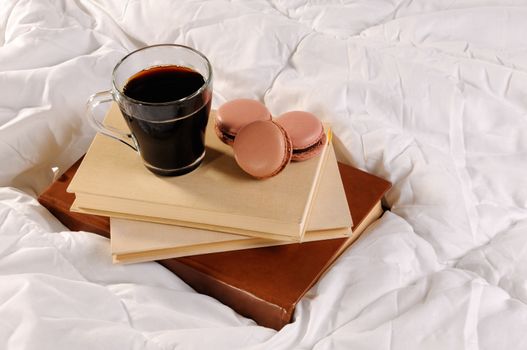 Morning cup of coffee with chocolate cakes Macaroons, on a pile of books in bed.
