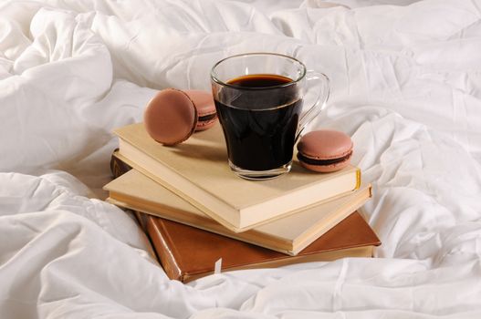 Morning cup of coffee with chocolate cakes Macaroons, on a pile of books in bed.