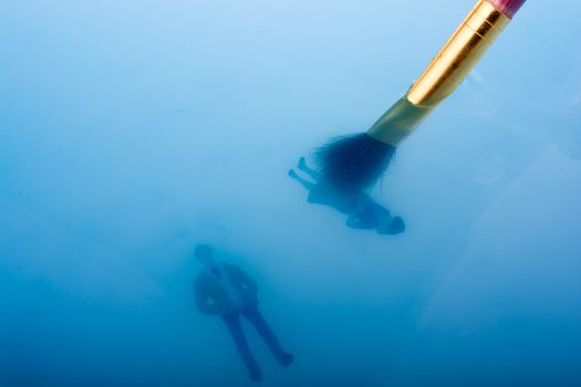 Painting brush and little floating figurines in blue water