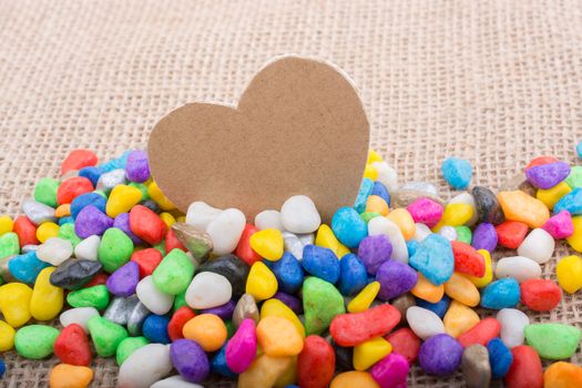 Paper heart amid colorful pebbles on canvas ground