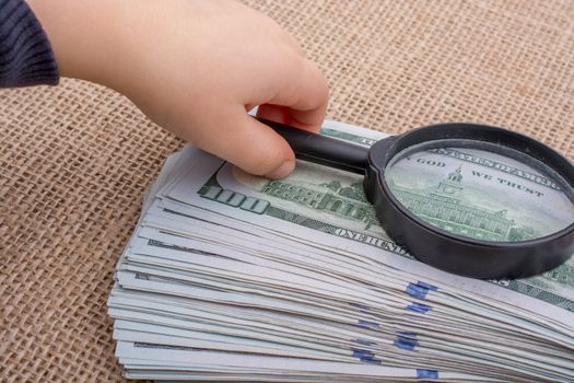 Toddler holding a magnifying glass  over the banknote bundle of US dollar