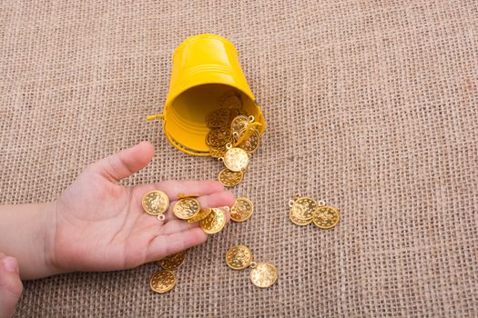 Bucket and fake gold coins in hand on canvas background