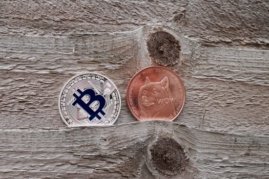 Digital currency physical silver bitcoin coin and brass dogecoin on wooden background.