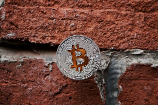 Digital currency physical silver bitcoin coin with yellow sign on the brick wall.