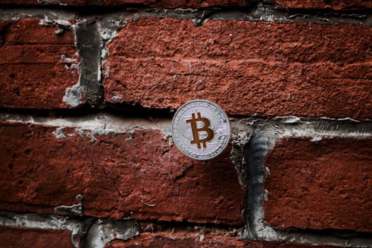 Cryptocurrency physical silver bitcoin coin with yellow sign on the brick wall.