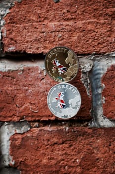 Gold and silver brexit coins on the brick wall. Europe leaving.