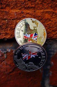 Two coins. Gold and silver brexit money with british map on brick wall.
