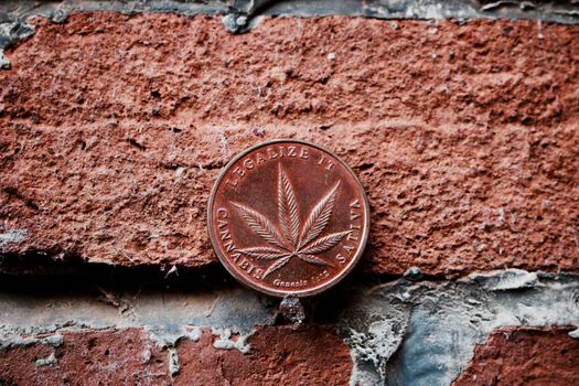 Legalize it. Sativa marijuana brass coin on the brick wall.