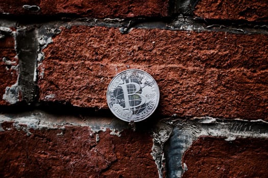 Digital currency physical silver bitcoin coin on the brown brick wall.