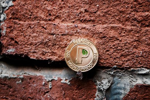 Digital currency physical gold peercoin coin with green leaf on the brick wall.