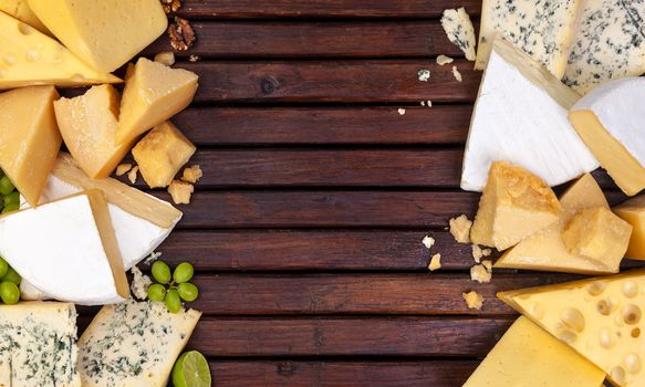Various types of cheese on wooden table background. Cheddar, parmesan, emmental, blu cheese. Top view, copy space.