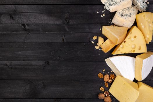 Various types of cheese on black wooden table background. Cheddar, parmesan, emmental, blu cheese. Top view, copy space.