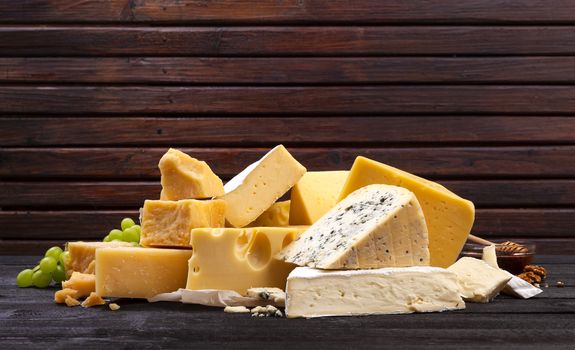 Various types of cheese on black wooden table background. Cheddar, parmesan, emmental, blu cheese. Copy space.