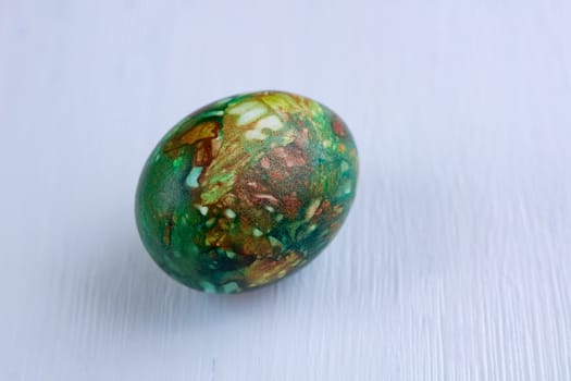 Multicolored green Easter holiday egg on white wooden natural background