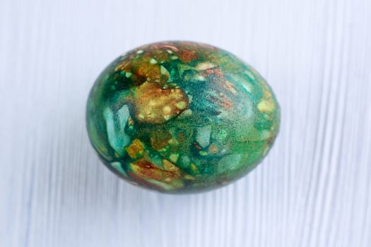 Multicolored green Easter holiday egg on white wooden natural background