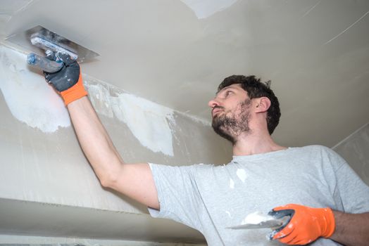 A worker with protective gloves is plastering the ceiling.