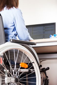 Invalid or disabled young business woman person sitting wheelchair working office desk computer