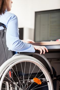 Invalid or disabled young business woman person sitting wheelchair working office desk computer