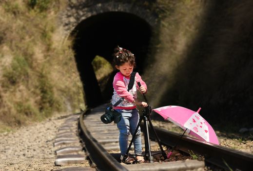 Little girl photographer with tripod and DSLR camera strapped on her shoulder.