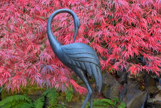 Bronze crane statue against red laced leaf maple trees in home garden backyard in fall season color