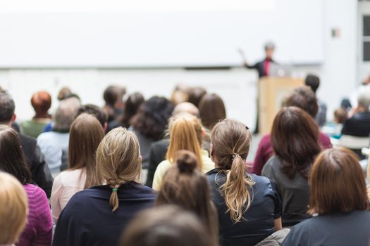 Female speaker giving presentation in lecture hall at university workshop. Audience in conference hall. Rear view of unrecognized participant in audience. Scientific conference event.