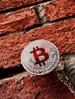 Digital currency physical silver bitcoin coin with red sign on brick wall.