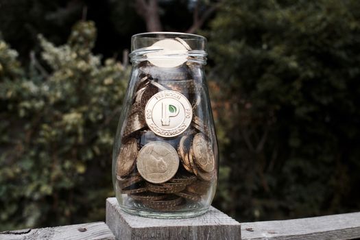 Digital currency physical gold peercoin coin with green sign. Transparent glass jar.