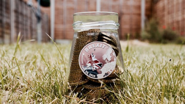 Europe leaving. Silver brexit coin on small glass jar in green garden.