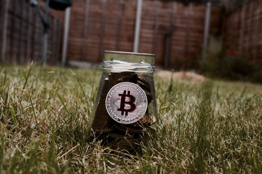 Digital currency physical silver bitcoin coin on glass jar in green grass.
