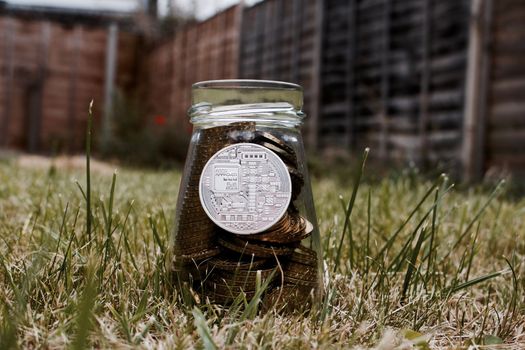 Digital currency physical silver bitcoin coin in glass jar on grass in garden.