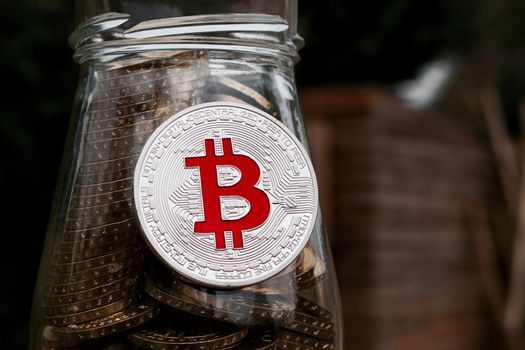 Digital currency physical silver bitcoin coin on glass jar with money.