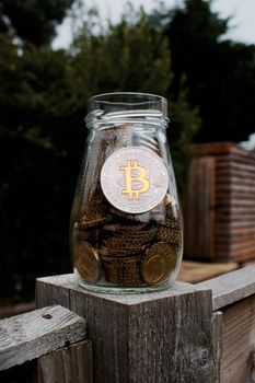 Digital currency physical silver bitcoin coin in glass jar outdoor.