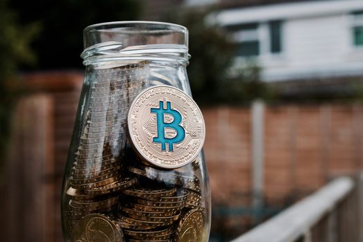Cryptocurrency physical gold bitcoin coin with blue sign on glass jar in garden.