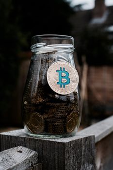 Digital currency physical gold bitcoin coin in glass jar in garden.