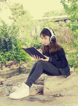 Young beautiful girl reading a book and 
listen to music in the park